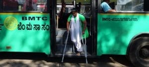 Woman with an above knee amputation stepping down from a bus using under arm crutches.