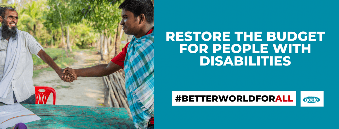 Two people are shaking hands. Each person has one arm amputated. Above the image of the two people is the text, “Sign the Petition.” Overlaying the image of the people is the text, “#BetterWorldForAll” and beside the text on the right side is the ADDC logo. The ADDC logo is composed of the letters “ADDC” on a teal background. At the bottom of the frame, the text, “Restore the budget for people with disabilities,” appears in white font on a teal background.